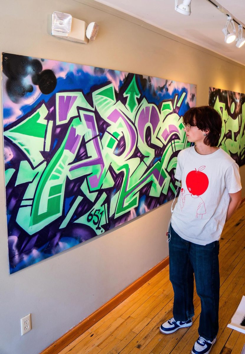 Ezra Young stands next to a piece of his art displayed at SPRAYFiNGER.